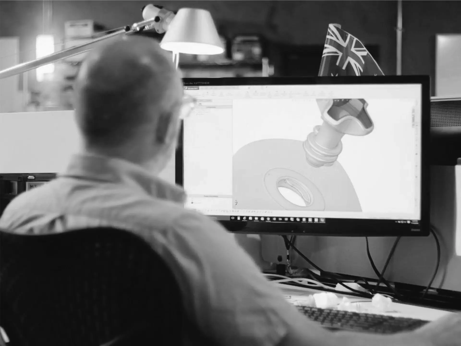 A designer reviewing a 3D CAD model of a part on a monitor
